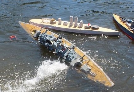 a model bismark rolls onto its side as it sinks from combat damage